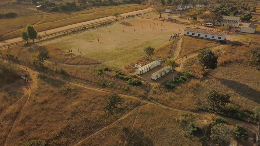 Slow Rising Shot Over a Soccer Game on a Dirt Field at a Rural Primary School in Zimbabwe, Africa to Reveal a Beautiful Mountain Landscape During Sunset | Shutterstock HD Video #1016180029