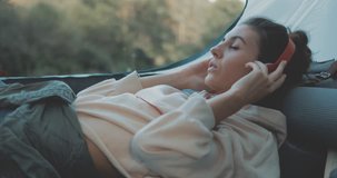 Young tourist on vacation in forest. Happy girl relaxing in camping tent. Hiker listen to music from the phone. People living healthy active lifestyle. 4K video shooting by handheld gimbal