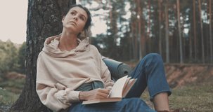 Attractive young woman reading a book outdoor in forest. Hiker camping in woods. 4K video shooting by handheld gimbal