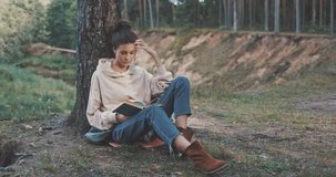 Attractive young woman reading a book outdoor in forest. Hiker camping in woods. 4K video shooting by handheld gimbal