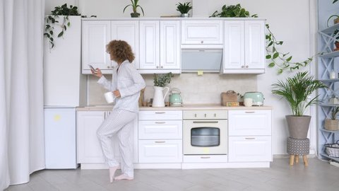 Young Woman Dancing And Using Cellphone In Kitchen.