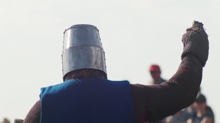 A man in mail, in armor, riding a horse welcomes the audience, waving his hand