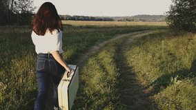 girl is running with a suitcase across the meadow. End of summer season, August.