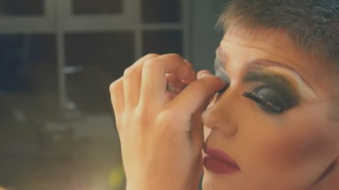 travesty-diva. The concept of a transvestite. Man-actor turns into a woman. a man applies a make-up on his face. in the room in front of the mirror. 4k, shooting steadicam