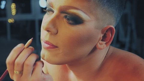travesty-diva. The concept of a transvestite. Man-actor turns into a woman. a man applies a make-up on his face. in the room in front of the mirror. 4k, shooting steadicam