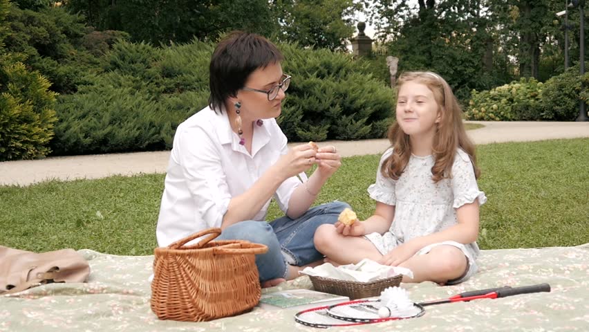 Happy Mother and Daughter eating a Cupcake on a Blanket at Park Picnic