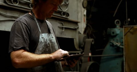 Attentive Caucasian blacksmith using digital tablet in workshop 4k
