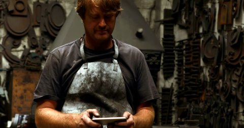 Attentive blacksmith using mobile phone in workshop 4k