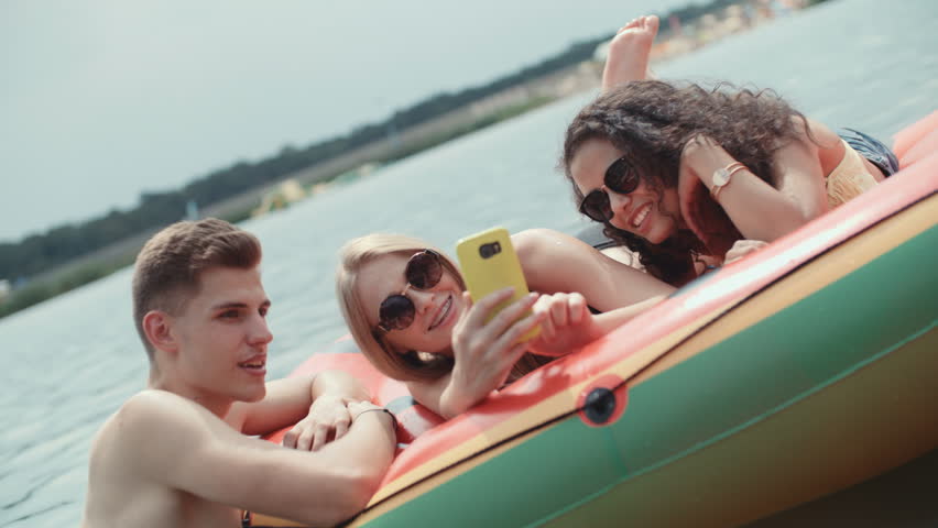 Cheerful friends spending time by the lake and using phone. Group of friends making selfies.