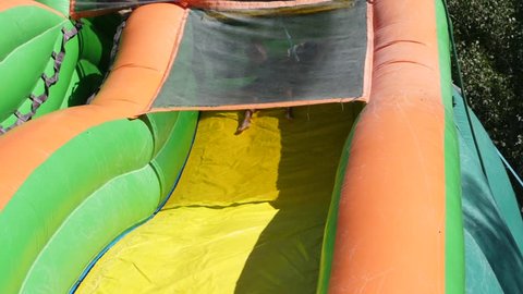 A slow motion shot of children playing and sliding down a large inflatable water slide