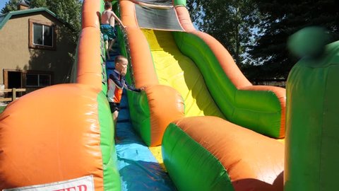 A slow motion shot of children playing and sliding down a large inflatable water slide