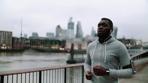 Young sporty black man runner with smart phone running on the bridge in a city.