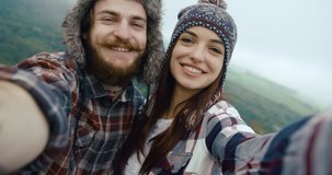Young hypster couple takes a video of themselves standing on the top of a rock with beautiful mountain view behind