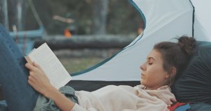 Young tourists couple in love on vacation in forest. Hiker girl reads book in camping tent. People living healthy active lifestyle. 4K video shooting by handheld gimbal