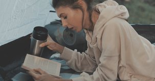 Young tourists couple in love on vacation in forest. Hiker girl reads book in camping tent. People living healthy active lifestyle. 4K video shooting by handheld gimbal