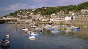 Slow elevated pan across the pretty harbour of Mousehole in Cornwall with colorful fishing boats moored