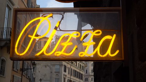 CLOSE UP: Vintage lettering glowing outside of a traditional pizza shop in Rome. Cool shot of retro yellow pizza sign shining brightly in an empty alley in a big city in Italy. Popular Italian food.