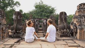 Young couple contemplating ancient temple in Cambodia, Angkor Wat  two people travel destinations Asia concept. 4K video tourist man and woman sitting on temple