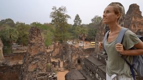 Young woman contemplating view at sunset from top of ancient temple in Cambodia 
4K video of tourist female solo traveler enjoying different cultures in Asia 