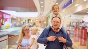 Happy family of four doing shopping. Family in mall. Children At Mall With Parents. Family shopping in big store. A Father Carries His child on His Shoulders and mom is holding a little daughter