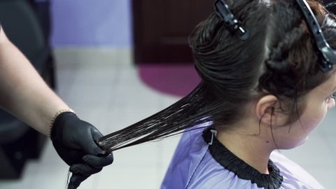 The hairdresser combs the client's wet hair after applying keratin, distributes the composition along the entire length of the hair with a comb. Close-up slow motion