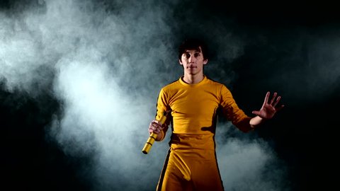 The man in  yellow suit practicing kung fu. Master holding nunchuck. Fighter isolated on black background. Concept of healthy life and martial arts. smoke. Bruce Lee style.