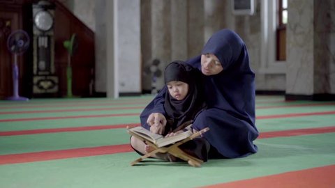 Asian Indonesian Muslim mother is teaching on how to read the quran to her daughter in the holy Mosque. Islam,religion and knowledge concept.