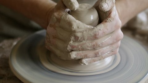 Close up of hands of unrecognizable male artisan shaping clay on spinning pottery wheel
