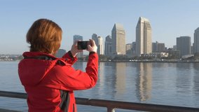 Woman traveler use phone taking street panoramic photo. Girl takes photos of downtown on mobile phone camera. Urban life concept. Mobile photograph and video of attractions in San Diego.
