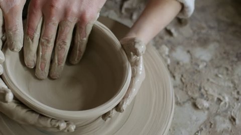 Top view with close up of hands of unrecognizable man and children throwing pot on spinning pottery wheel and failing