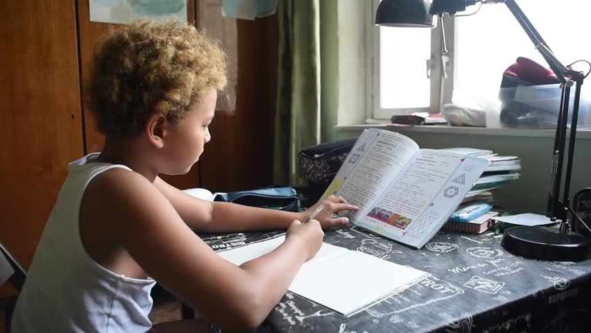 Schoolboy doing homework in his room in the home. Cute african american boy sitting  at the table and thinking and writing in his notes. Home education for kids.  Boy learning something from his book. Royalty-Free Stock Footage #1016284615