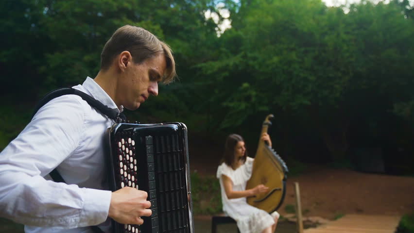 Two musicians Pianist and bandurist playing on the rocks at waterfall