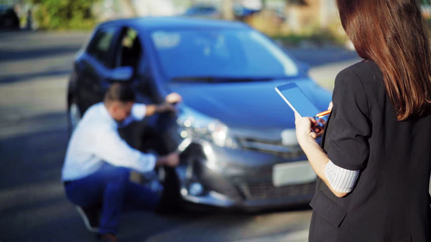 Insurance concept. Female insurance agent inspects damage to a man's car and makes notes on a tablet computer, during discussion with man. Woman with digital tablet inspecting broken car. 4K UHD. Royalty-Free Stock Footage #1016291104