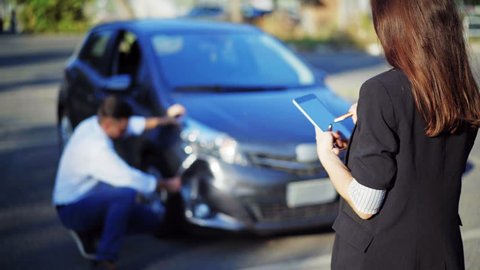 Insurance concept. Female insurance agent inspects damage to a man's car and makes notes on a tablet computer, during discussion with man. Woman with digital tablet inspecting broken car. 4K UHD.