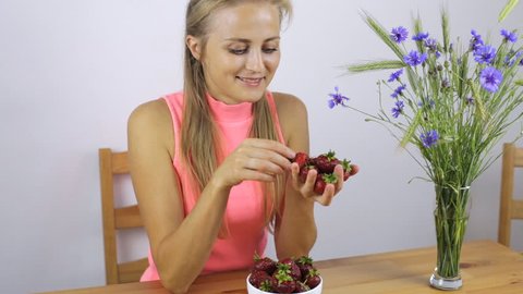 Woman sitting in the kitchen eating strawberries