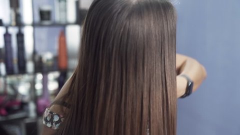 A close-up slow-motion shot of a girl in a beauty salon admires her long straight shiny hair after keratin straightening. The concept of hair care in the salon, keratin, hair straightening.