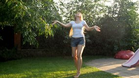 4k video of cheerful laughing young woman dancing under summer rain on sunset at house backyard