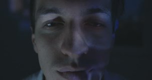 Close up of young man watching a video or film on TV or a computer monitor at home. Reflection on his face.