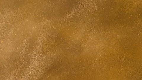 Gold ink in water shooting with high speed camera. Golden glitter sand or dust creating abstract cloud formations metamorphosis. Art backgrounds. Macro view.