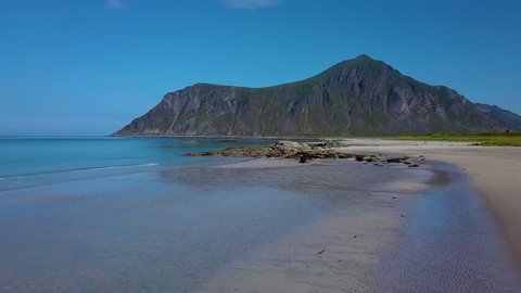 A flight over a sandy beach and a stone cape. The beautiful coast of Lofoten. Clear water and a mountain on the horizon. Norway
