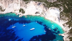 Aerial drone bird's eye view video of sail boats docked in tropical caribbean paradise bay with white rock caves and turquoise clear sea