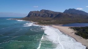 Aerial of waves breaking on pristine beach with lagoon & mountains in background, Kleinmond, South Africa
