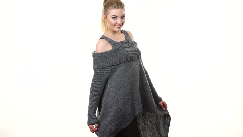 Happy blonde woman wearing fashionable grey long sleeve cold shoulder jumper woolen sweater, attractive model presenting clothing moves for camera on white
