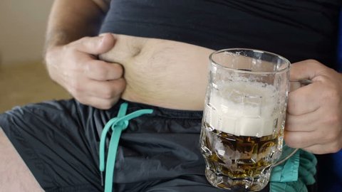 The fat man drinks beer. A man is ironing a beer belly. Bad food, gluttony. Close-up