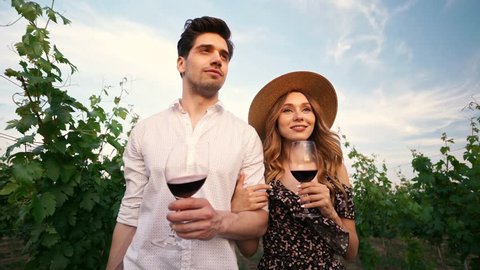 Young happy loving couple walking outdoors in the vineyard talking with each other drinking wine