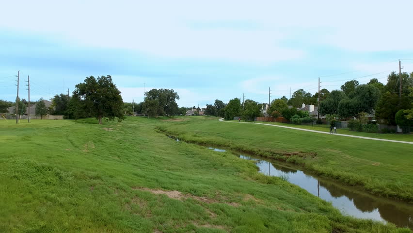 Aerial footage of activity on a neighborhood biking trail running along a large retention pond and drainage canal that is part of flood control for a large suburban area.