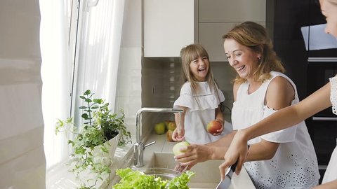 Young caucasian mother with her daughter is having fun splashes each other water in the kitchen and wash the vegetables for ready to cook salad for lunch, slow motion