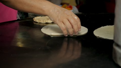 Close up of a woman's hand flipping a handmade corn tortilla on a metal pan or comal