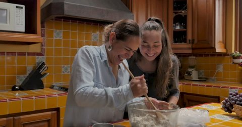 Genuine moment between a hispanic mother and mixed ethnic daughter laughing and cooking together - push in gimbal shot