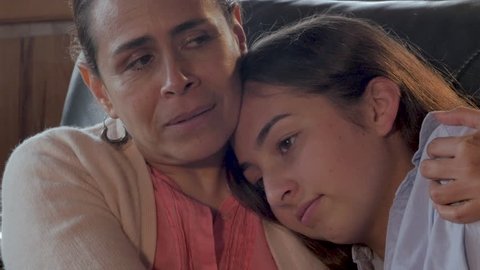 Attractive Mexican mother comforting her mixed race teenager child with her arm around her shoulder - close up